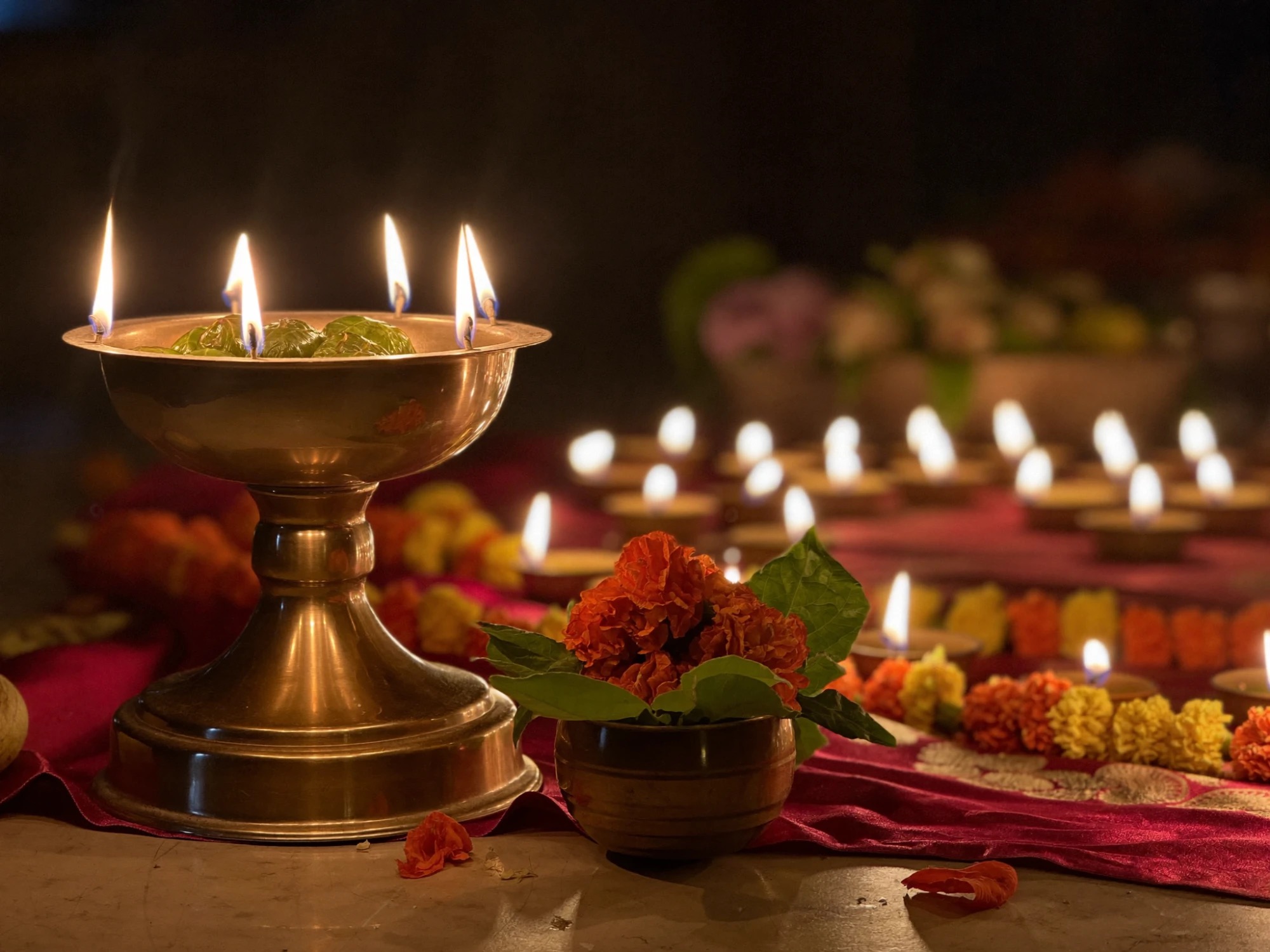 A brass diya with lit wicks beside marigold flowers and rows of oil lamps, set for Navratri Devi worship